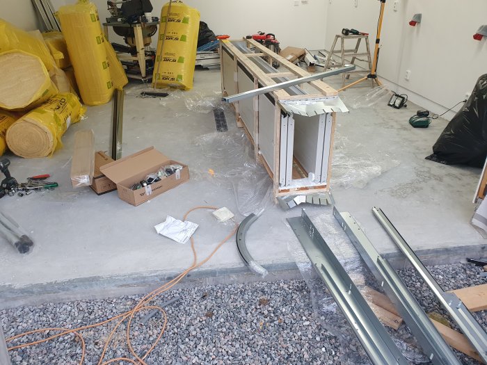 Byggmaterial och verktyg utspridda i garage under renovering med isolering och konstruktionsdelar.