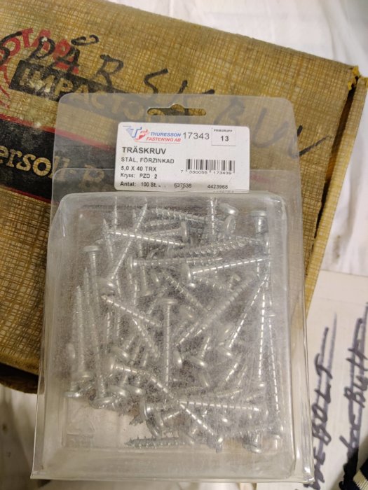Förpackning med förzinkade träskruvar på en suddig bakgrundsyta, märkt med storlek 5,0 x 40 TRX.