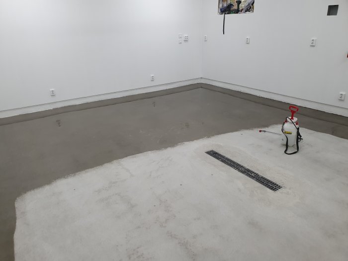 En nyslipad betongplatta i ett garage med nymålade vita väggar, eluttag och en tryckspruta på golvet.