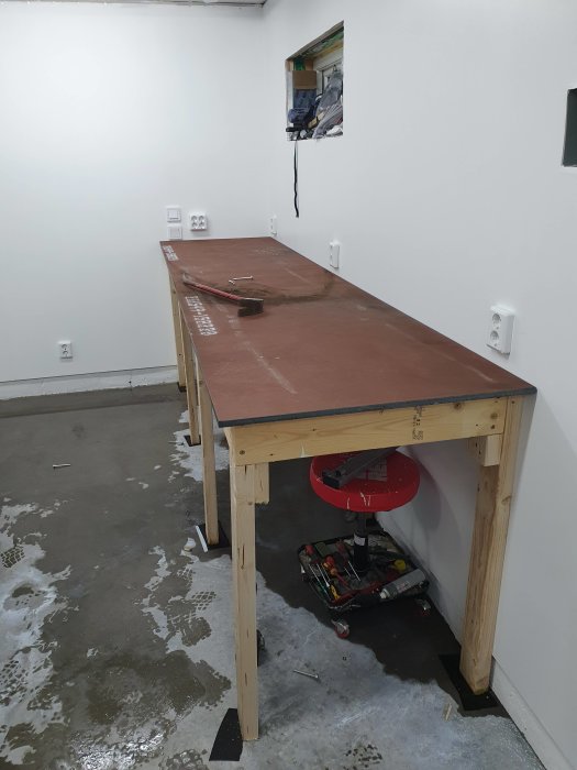 Hantverksbord med brun skiva och trästomme i ett nymålat garage med verktygslåda och verktyg under.