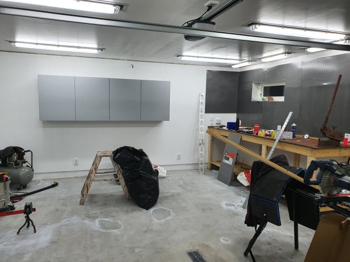 Renoverat garage med belysning, arbetsbänk, verktyg och grå skåp på väggen.
