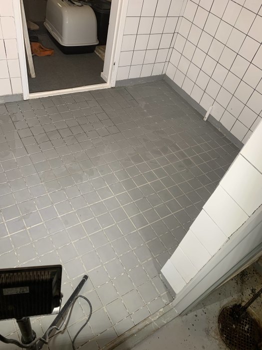 Nyinstallerade små klinkerplattor på ett källargolv med viss lutning och en brunnskant.