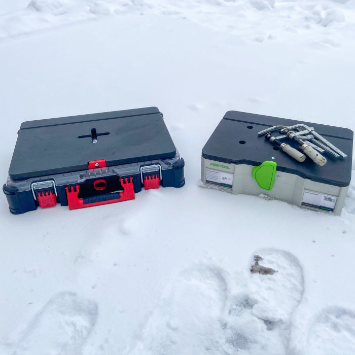 Två bärbara arbetsstationer i snö, en märkt Milwaukee Packout och en Festool med borrbitar på toppen.