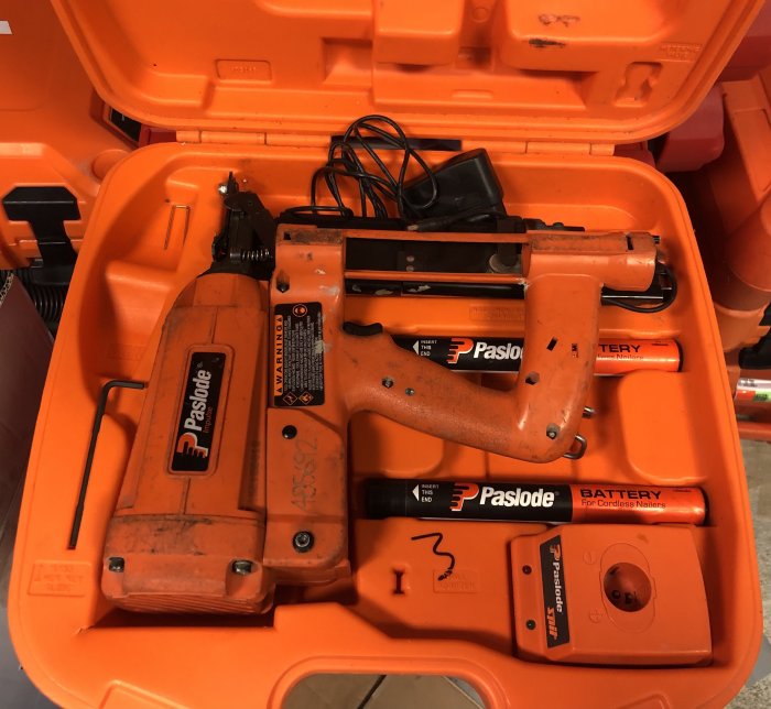 Paslode spikpistol och batteri i en öppen orange förvaringsväska, inköpt från Klaravik och Blocket.