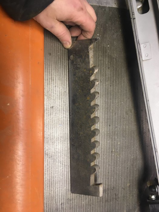 Hand håller i en metallstång med tänder på ett glidbord, möjligt tillbehör till snickerimaskin.
