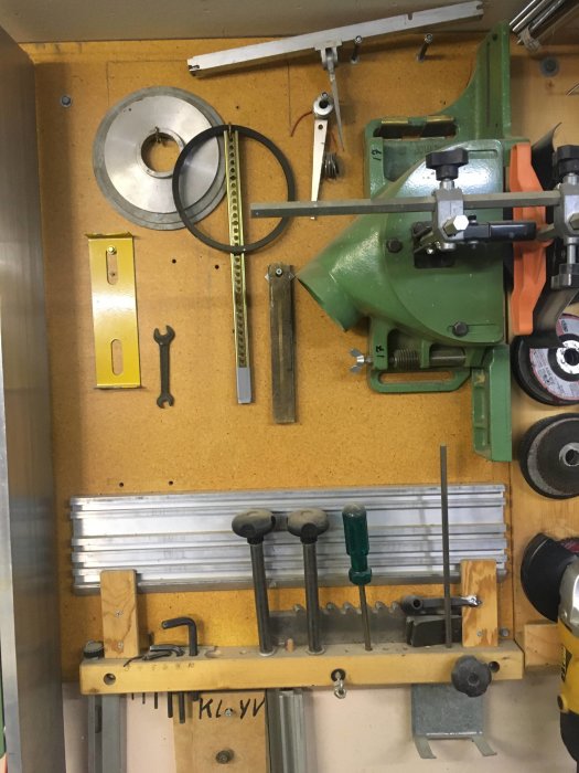 Verkstadspanel med olika verktyg och tillbehör inklusive en grön maskin och guider för träbearbetning.