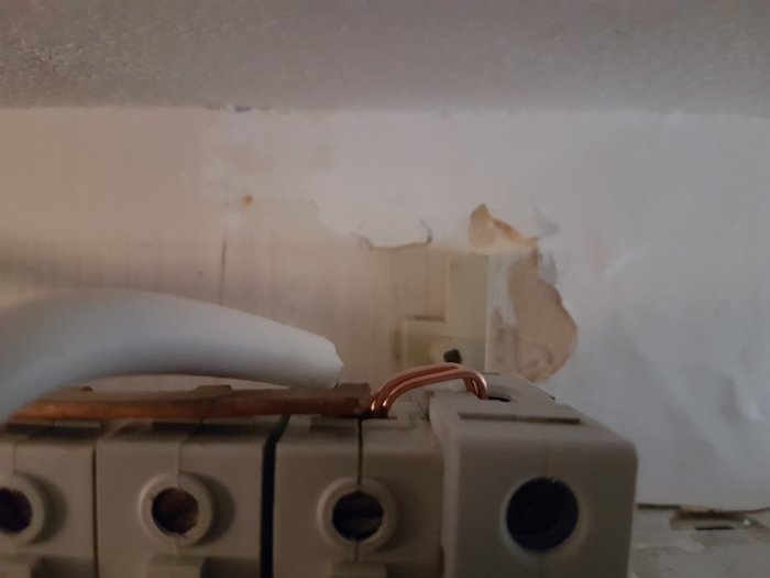 Elektrisk brytare på vägg med löstaget kåpa och synlig fasskena, slitage och skador på väggen.