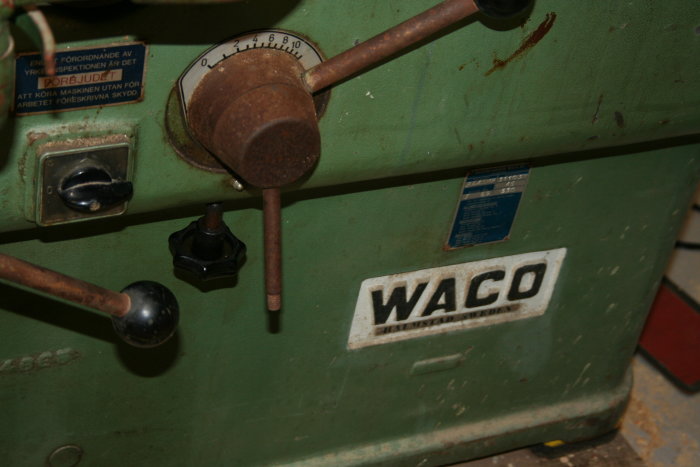 Närbild på del av en grön Waco trähövlingsmaskin med reglage och en varningsetikett.