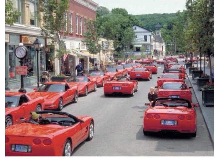 Rad av röda sportbilar köandes på en pittoresk stadsgata.
