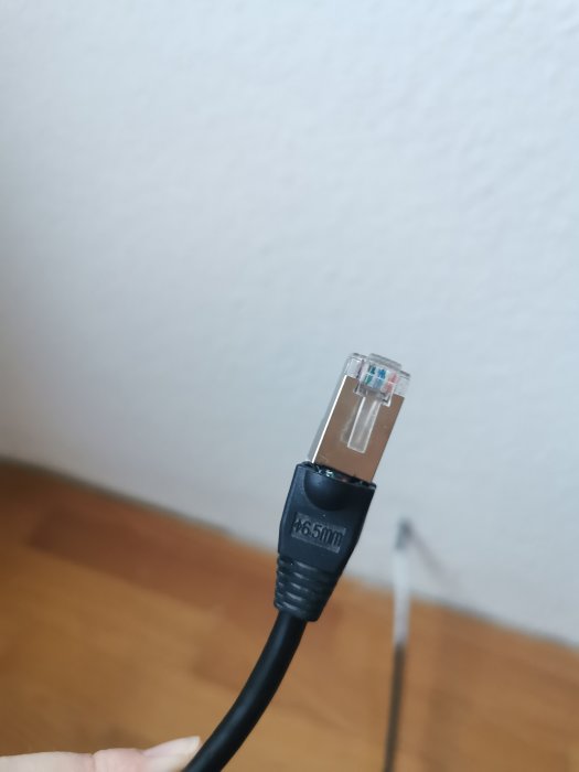 Närbild av en nätverkskabel (RJ45-kontakt) hållen i hand framför en vägg.