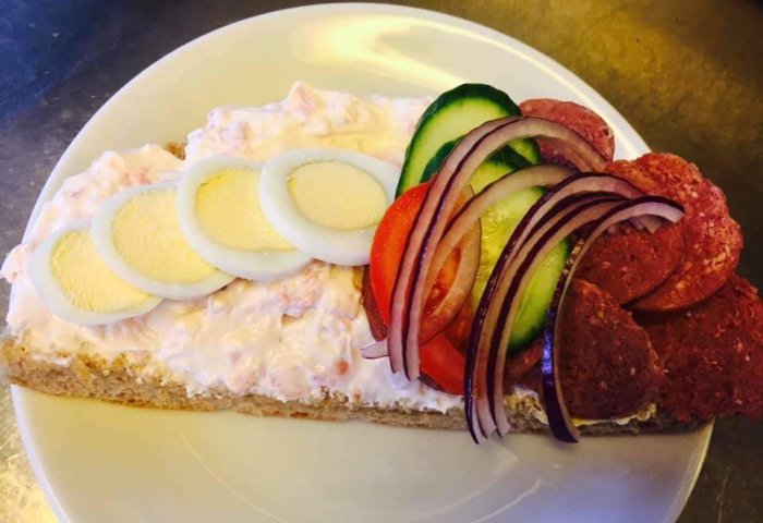 En rikligt toppad cafésmörgås med lager av hästkorv, räksallad, kokta äggskivor, tomat, gurka och rödlök.