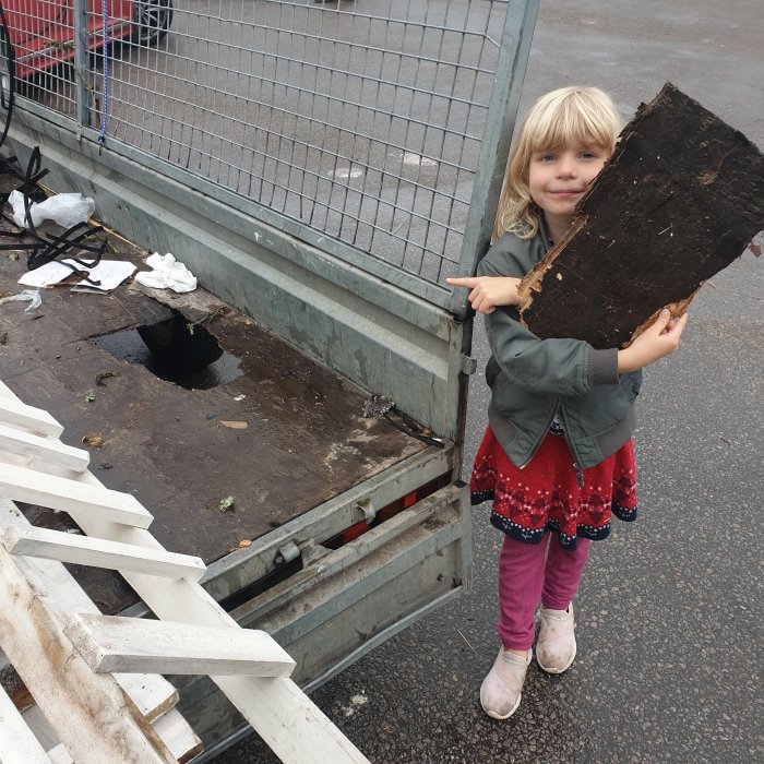 Barn håller en stor träskiva bredvid en släpkärra med tydlig skada i botten.