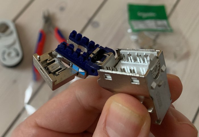 Bild på en hand som håller ett öppet RJ45 CAT 6A STP modulärjack framför verktyg och förpackning.