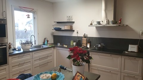 Kök med hyllor monterade med dolda konsoler, betsade i mörk ton, och bänkskivor med köksredskap.