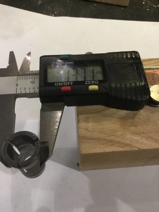 Digital skjutmått som visar måttet 41,1 mm bredvid en metallhylsa och ett träblock.