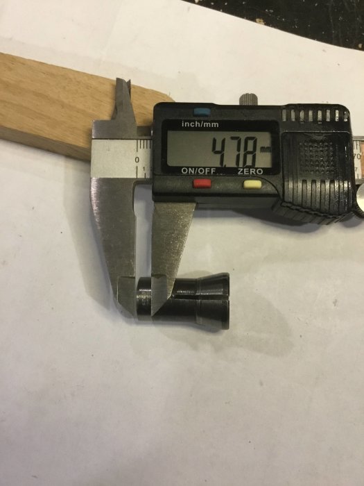 Skjutmått visar mätning av en metallhylsa med diametern 47,18 mm på ett vitt papper.