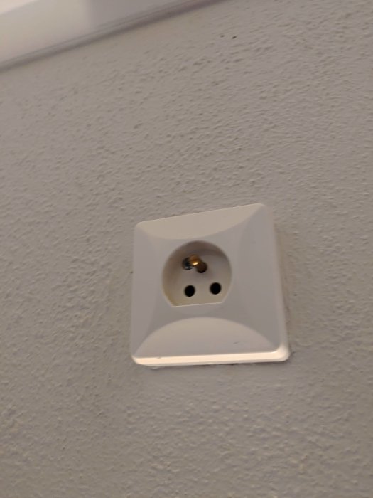 Vit jordad väggkontakt på en strukturerad grå vägg, med fråga om att koppla in ojordad lampa.