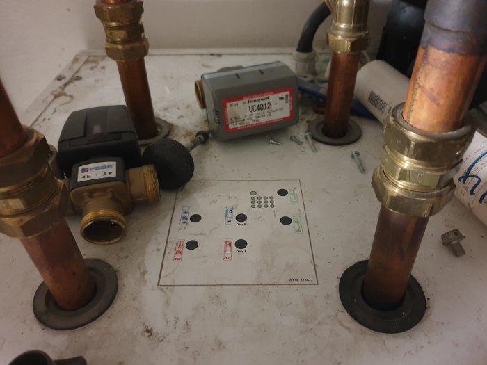 Rörledningar och ventiler med etiketter IN och UT samt en IVT E14 värmepumpskontrollpanel.