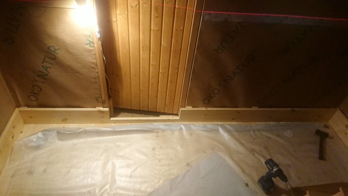 Installation av bastupanel med laserlinje, dyckertpistol och obehandlat trä i en hörna av bastun.