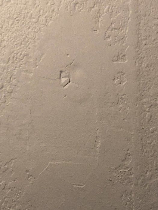 Ojämnt spacklad och skadad vägg med synliga sprickor och avflagnad färg.
