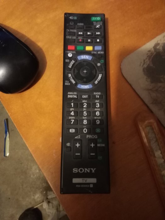 Sony TV-fjärrkontroll på ett bord intill en datormus och några lösa föremål.