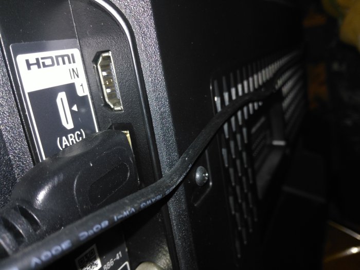 HDMI-kabel ansluten till HDMI IN-port på TV, omgivet av andra anslutningar och kontroller.