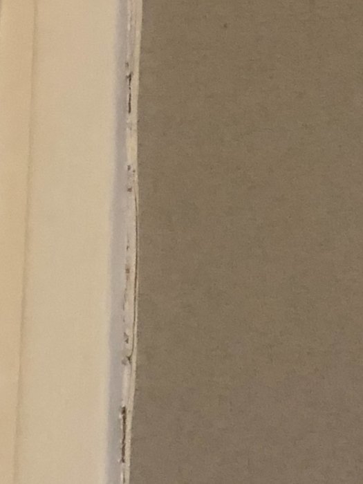 Vägg med dåligt spacklat hål och beskuren tapet vid en list.