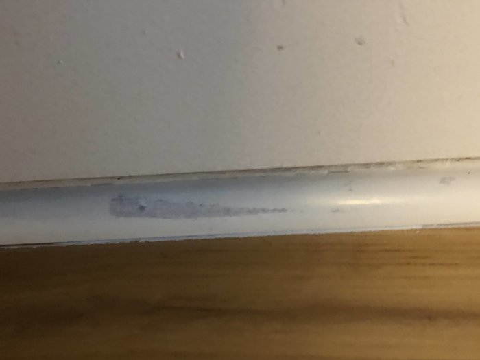 Något missfärgad och ojämnt övermålad golvlist mot en vit vägg med synliga spår av slarvigt måleri.