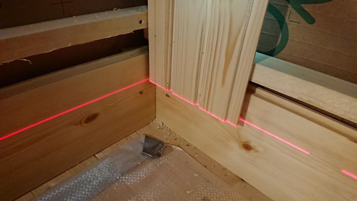 Installation av bastupanel nära dörren med en synlig laserlinje som hjälper till att säkerställa rätt vinkel och avstånd.