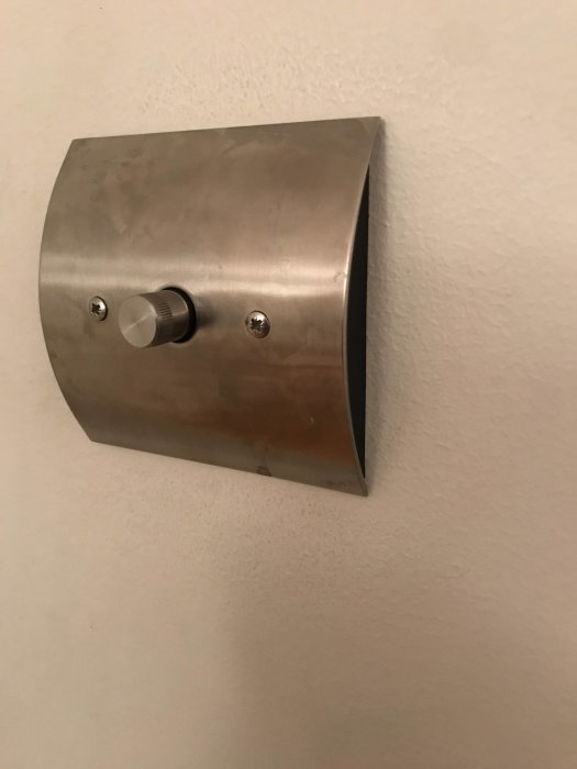 Bild på en väggmonterad strömbrytare med borstad metallfinish och en rund vridknapp.