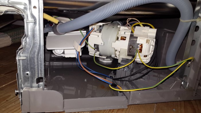 Diskmaskins inre med öppen sockelplåt som visar elektriska ledningar och mekaniska komponenter.