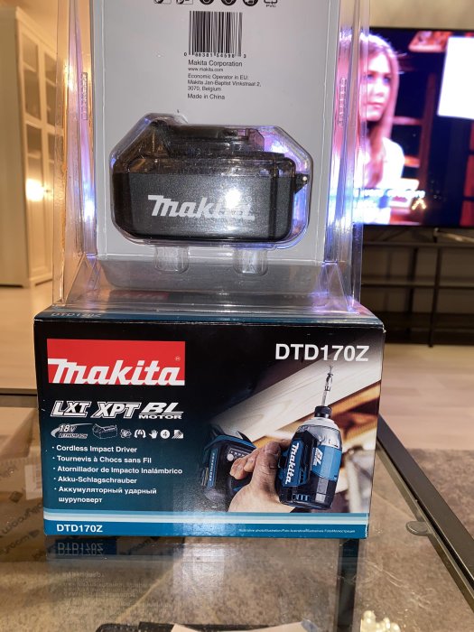 Ny Makita slagskruvdragare modell DTD170Z i förpackning på ett bord med suddig TV-skärm i bakgrunden.