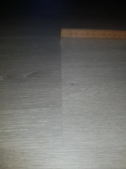 Nylagt laminatgolv med synlig glipa bredvid ett tumstock placerad för mätning.