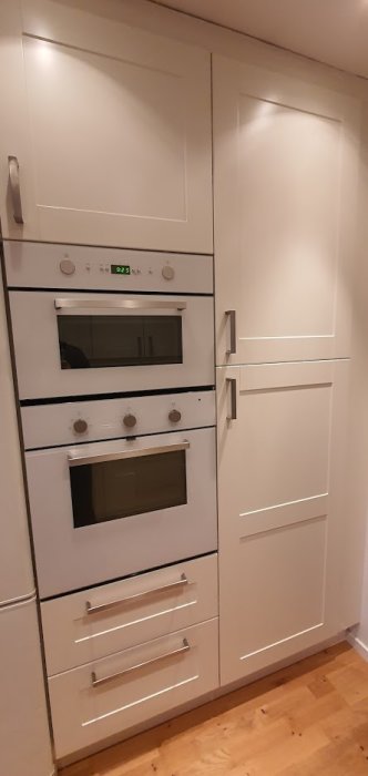Vit köksinredning med inbyggda ugnar och närliggande skåp, synliga tecken på luftläckage.