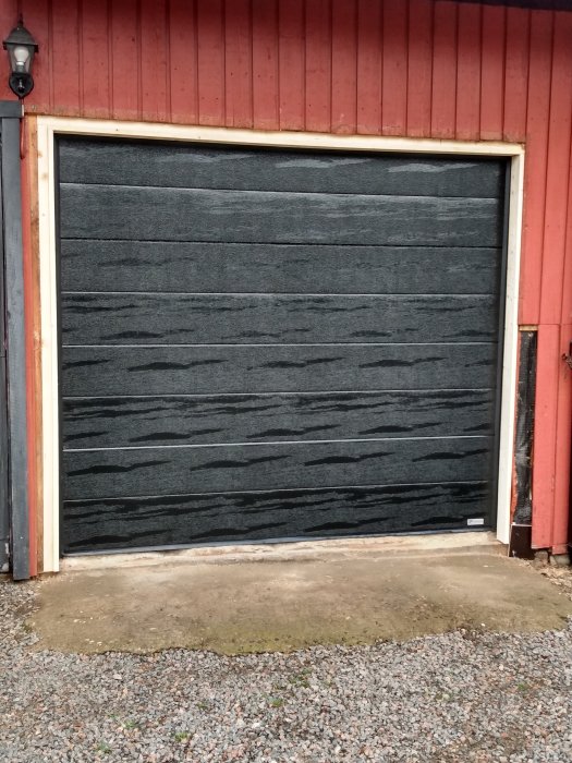 Nymålad garageport omgiven av orört träfoder på en röd byggnad, väntar på panelbyte.