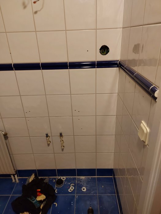 Renoveringsprocess i badrummet med borttaget innehåll och nerputsat kakel, verktyg och skräp på golvet.