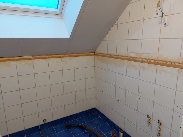 Renoverat badrum före renovering med kakelväggar, blå golvplattor och omala ytor.