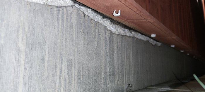 Betongvägg och träpanel med möjlig fuktskada och vit avlagring eller saltutslag.