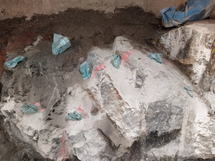 Bild på ett gruvområde med markerade borrställen och borrade hål, med blå plastskydd och röd markeringsspray.