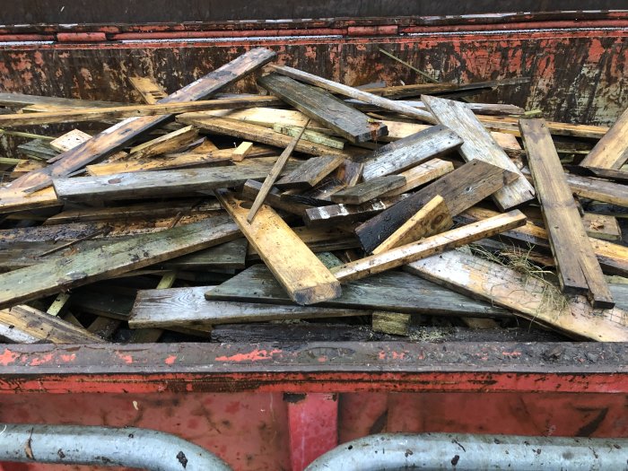 En hög med organiskt behandlat träavfall i en sliten röd container.