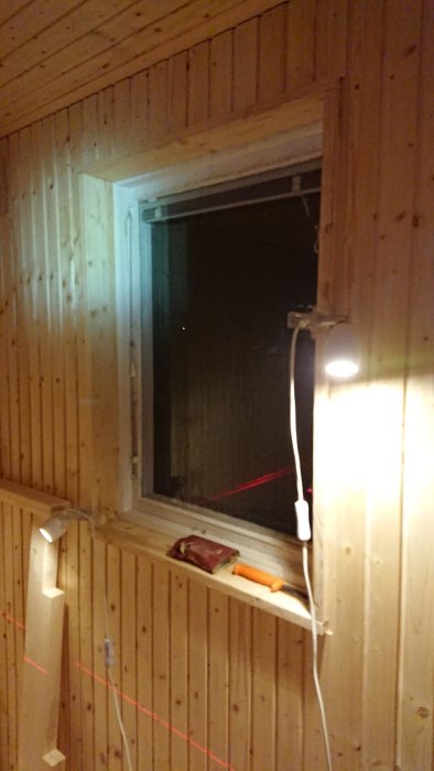 Interiörbild av en bastu under konstruktion med träpanel på väggarna, ett fönster och en utritad plan för ytterligare arbete.