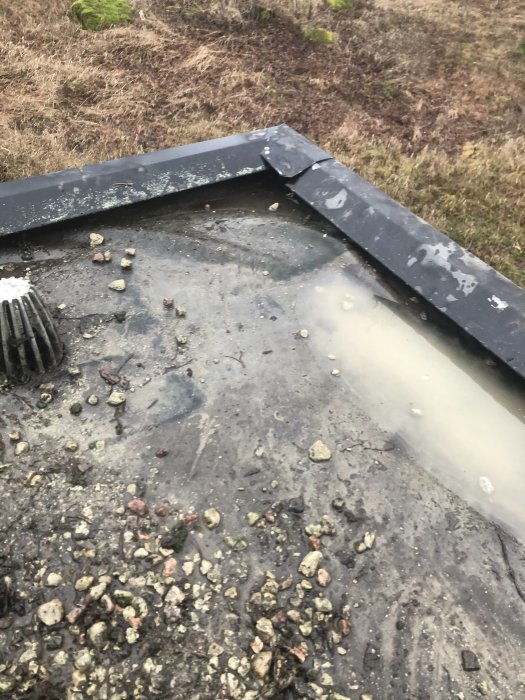 Hörn av ett platt garagetak med stillastående vatten och lös vindskiveplåt, tecken på potentiella vattenskador.