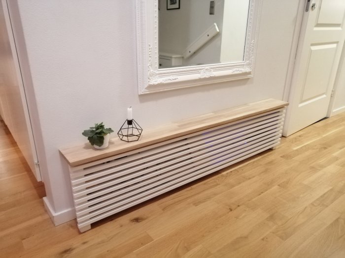 Nyinstallerad radiatorinklädnad i trä med dekorativ spegel och inredningsdetaljer på väggen ovanför.