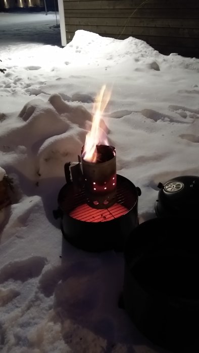 Chimneystarter med ovanligt höga lågor tänd på en snötäckt mark i mörkret.