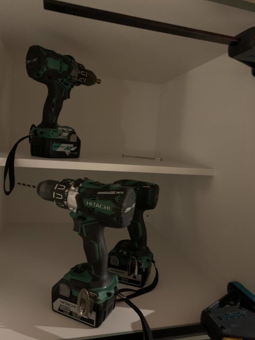 Två Hikoki/Hitachi borrskruvdragare på en hylla med batterier och laddare.