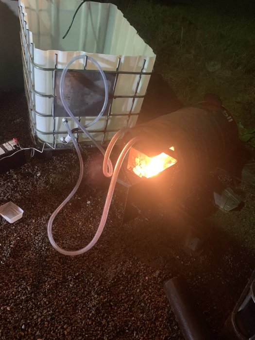 IBC-container som lutats för uppvärmning med ansluten vedeldad kamin och slangar för vattenflöde.