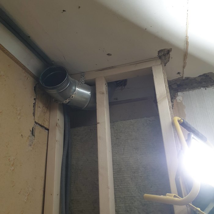 Ventilationsrör installerat i träram i en vägg under renovering med osynlig isolering och kablar.