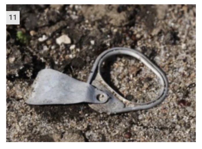 Gammal nyckelring av metall liggande på grusig mark.