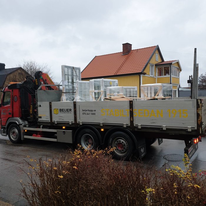 Lastbil från Beijer Byggmaterial levererar nya fönster och dörrar till ett gult hus.