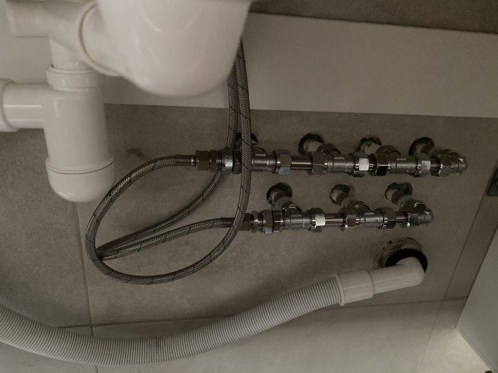VVS-installation under handfat med rörkopplingar och flexibla slangar.